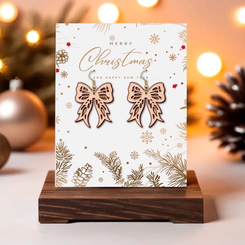 May include: Wooden bow-shaped earrings with gold-colored hooks are displayed on a Christmas-themed card. The card reads "Merry Christmas and Happy New Year" with festive illustrations. The earrings are on a dark wooden stand.