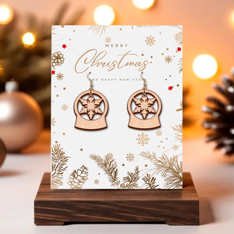 May include: Wooden snowflake earrings displayed on a Christmas-themed card. The earrings are light brown, shaped like snow globes with snowflake cutouts. The card reads "Merry Christmas and Happy New Year" with gold accents and snowflake illustrations. The earrings are on a wooden stand.