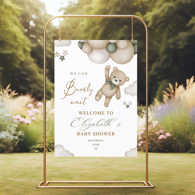 May include: A baby shower welcome sign in a gold frame. The sign features a teddy bear illustration with the text "We can bearly wait" and "Welcome to Elizabeth's Baby Shower". The background includes clouds and stars.