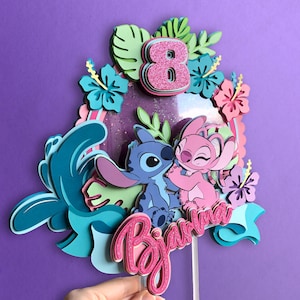 May include: A layered cake topper featuring the characters Stitch and Angel, with a pink glitter number 8 and the name "Biana". The design includes tropical flowers and foliage in shades of blue, pink, and green, set against a purple background.