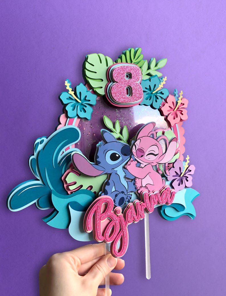 May include: A layered cake topper featuring the characters Stitch and Angel, with a pink glitter number 8 and the name "Biana". The design includes tropical flowers and foliage in shades of blue, pink, and green, set against a purple background.