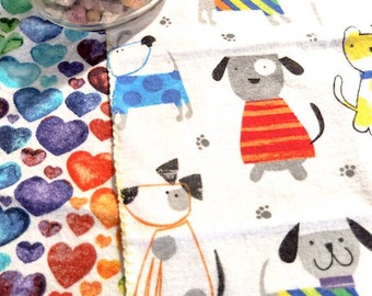 Könnte beinhalten: Weißer Stoff mit einem sich wiederholenden Muster aus bunten Hunden, die verschiedene Outfits tragen. Die Hunde schauen alle nach vorne und haben schwarze Augen und Nasen. Der Stoff ist mit einer gelben Naht eingefasst.