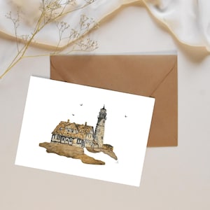 May include: Watercolor art print of a lighthouse and adjacent building on a rocky outcropping. The buildings have a stone and brown roof. The print is on white paper, with a brown envelope behind it. A sprig of dried flowers is in the upper left corner.