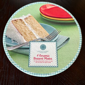 May include: A set of four 7-inch ceramic dessert plates with a green background and a white and blue checkered border. The plates are designed for decorating a piece of cake. The image also shows a slice of cake with white frosting and a fork on a blue plate.
