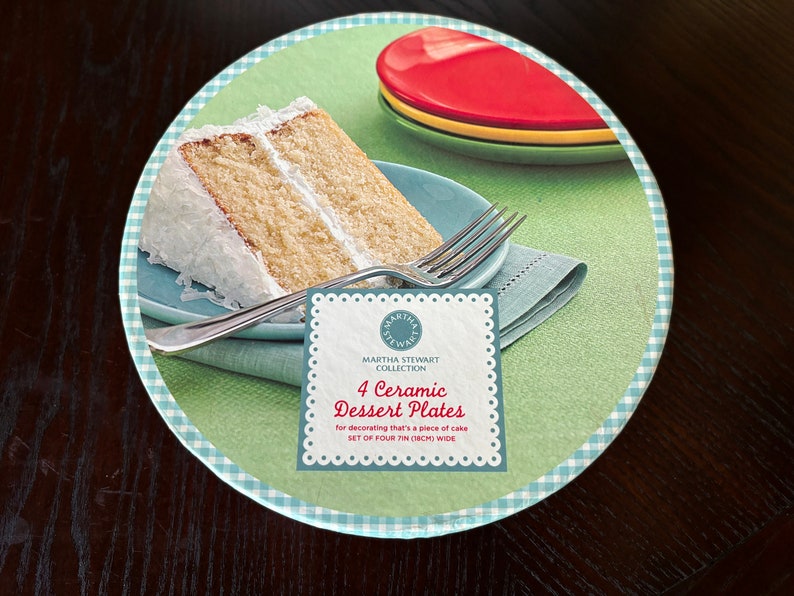 May include: A set of four 7-inch ceramic dessert plates with a green background and a white and blue checkered border. The plates are designed for decorating a piece of cake. The image also shows a slice of cake with white frosting and a fork on a blue plate.