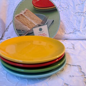 May include: A set of four ceramic plates in yellow, red, green, and blue. The plates are stacked on top of each other. The image shows a close-up of the plates.