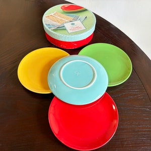 May include: Four colorful ceramic dessert plates in yellow, blue, green, and red. The plates are stacked on top of each other. The plates are part of a set of dessert plates.