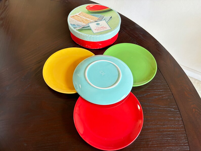 May include: Four colorful ceramic dessert plates in yellow, blue, green, and red. The plates are stacked on top of each other. The plates are part of a set of dessert plates.