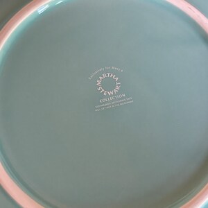 May include: A light blue ceramic plate with a white rim. The bottom of the plate has a white logo that reads "Exclusively for Macy's Martha Stewart Collection Dishwasher/Microwave Safe Will Get Hot in the Microwave".