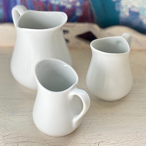 May include: A set of three ceramic mugs with a speckled, matte finish. The mugs are in shades of cream, light gray, and dark gray. Each mug has a simple, minimalist design, perfect for coffee or tea.