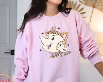 May include: Pink sweatshirt with a cartoon image of Mrs. Potts and Chip from Beauty and the Beast. The image is in a vintage style with gold accents and stars.