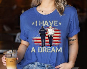 May include: Blue t-shirt with the text "I HAVE A DREAM" and an illustration of a police officer escorting a man in front of an American flag. The shirt has rolled-up sleeves.