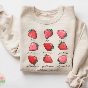 Puede incluir: Una sudadera beige con un gr&aacute;fico de fresas y el texto "love, joy, peace, forbearance, kindness, goodness, faithfulness, gentleness, self-control, Galatians 5:22-23".