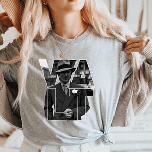 Puede incluir: Camiseta gris de manga larga con una imagen en blanco y negro de un hombre con traje y sombrero. La palabra "WALT" est&aacute; impresa en letras blancas sobre la imagen. La camiseta es de material suave.