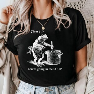 May include: Black t-shirt featuring a frog chef stirring a pot, with the text "That's it. You're going in the SOUP." The frog wears an apron. The design is in white.
