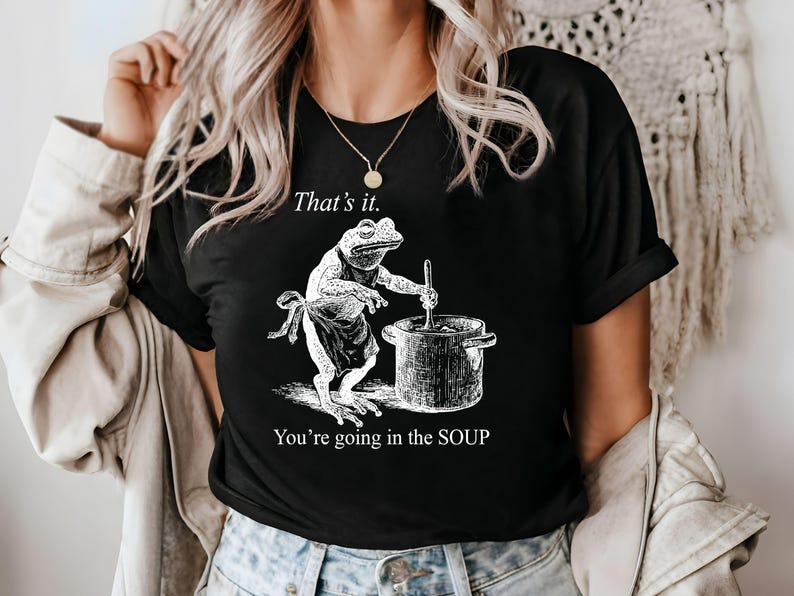 May include: Black t-shirt featuring a frog chef stirring a pot, with the text "That's it. You're going in the SOUP." The frog wears an apron. The design is in white.