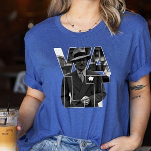 Puede incluir: Camiseta azul real con una imagen en blanco y negro de un hombre con traje y sombrero, con el nombre "WALT" en letras blancas. Las mangas est&aacute;n dobladas.