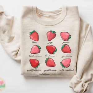 Puede incluir: Una sudadera beige con un gr&aacute;fico de fresas y el texto "love, joy, peace, forbearance, kindness, goodness, faithfulness, gentleness, self-control, Galatians 5:22-23".