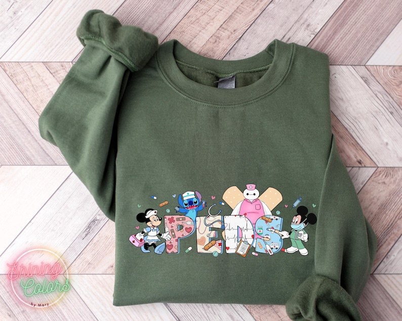 May include: Green sweatshirt with a graphic print of Disney characters dressed as nurses. The characters include Stitch, Mickey Mouse, Baymax, and a nurse Minnie Mouse. The text "NURSES" is spelled out with medical symbols and bandages.