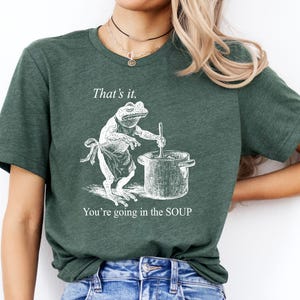 May include: Dark green t-shirt with a humorous graphic of a frog stirring a pot of soup. The text above the frog reads "That's it." and below it says "You're going in the SOUP."