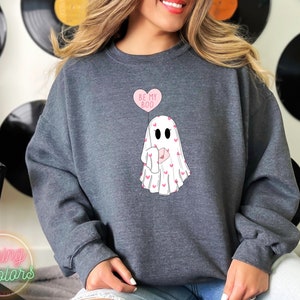 May include: A dark grey sweatshirt with a white ghost holding a pink heart balloon that says "Be My Boo". The ghost is surrounded by small pink hearts.
