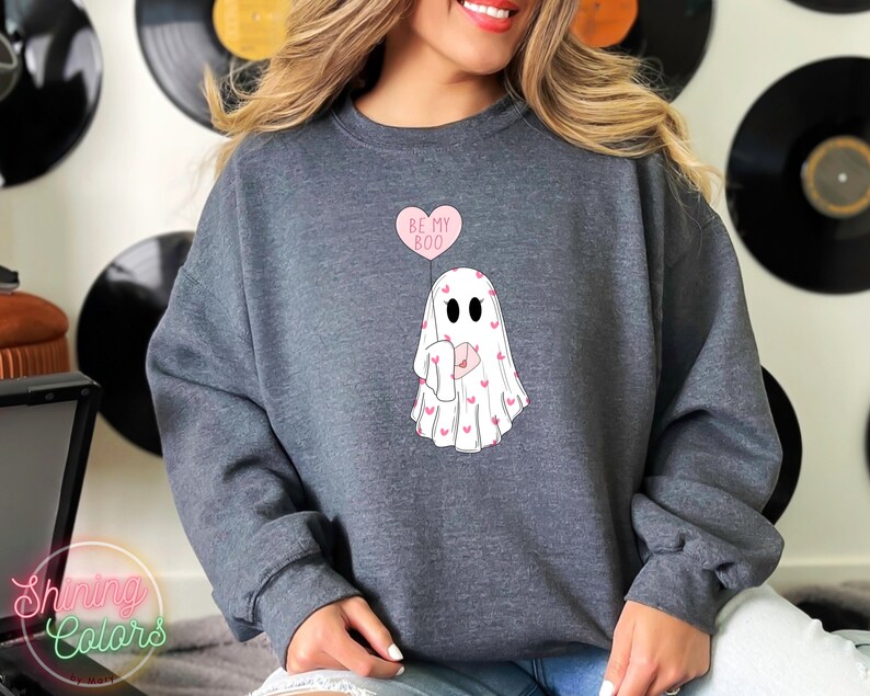 May include: A dark grey sweatshirt with a white ghost holding a pink heart balloon that says "Be My Boo". The ghost is surrounded by small pink hearts.