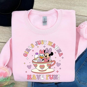 Puede incluir: Sudadera rosa con un gr&aacute;fico de Minnie Mouse y Daisy Duck en una taza de t&eacute;. El texto "Girls Just Wanna Have Fun!" est&aacute; impreso debajo de la imagen.