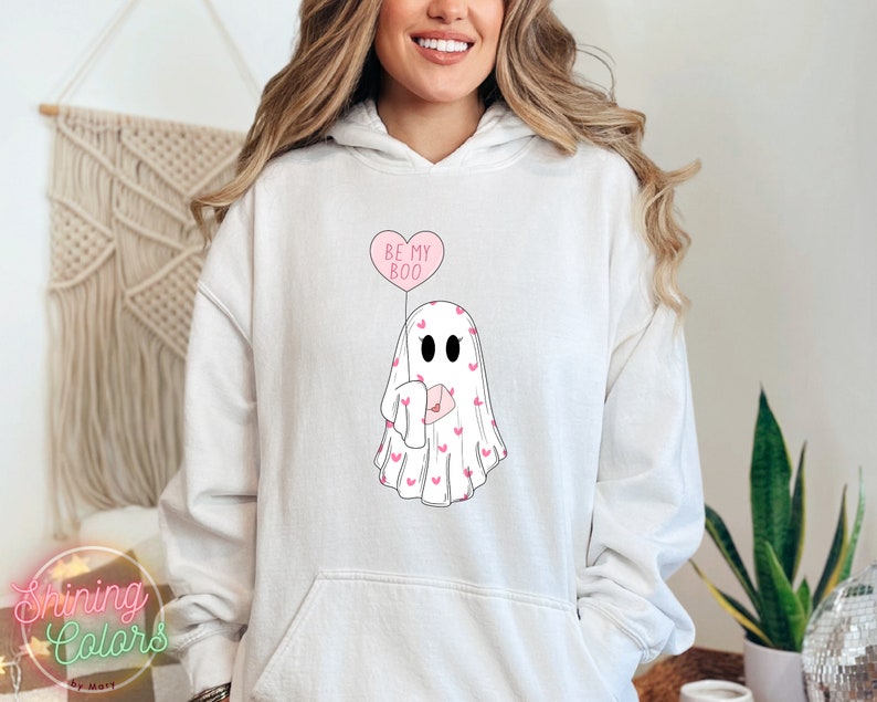 May include: White hoodie with a pink ghost holding a pink heart balloon that says "Be My Boo". The ghost is covered in small pink hearts.