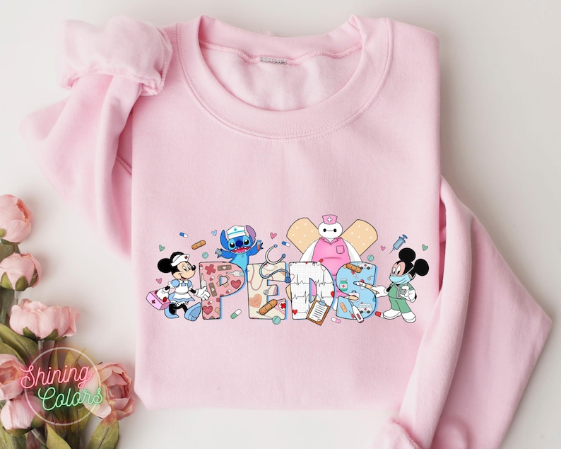 May include: Pink sweatshirt with a graphic of Stitch, Mickey Mouse, and Baymax dressed as nurses. The graphic includes the word "PEDS" in a colorful, medical-themed design.