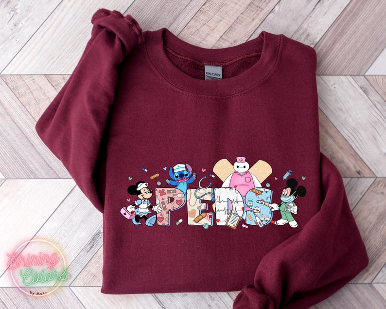 May include: Burgundy sweatshirt with a graphic of Disney characters dressed as nurses. The characters include Stitch, Mickey Mouse, Minnie Mouse, and Baymax. The text "Peds" is written in a colorful font.