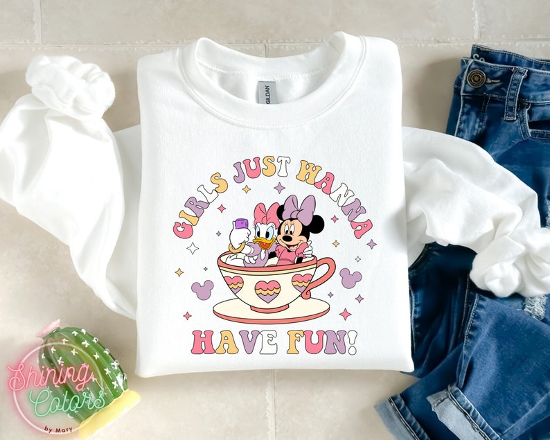 Puede incluir: Sudadera blanca con un gr&aacute;fico rosa, amarillo y azul de Minnie Mouse y Daisy Duck en una taza de t&eacute;. El texto "Girls Just Wanna Have Fun!" est&aacute; impreso en una fuente retro.