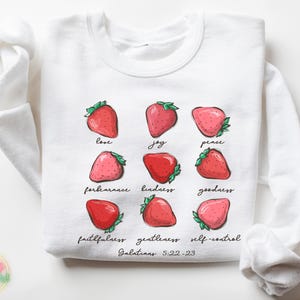 Puede incluir: Sudadera blanca con un gr&aacute;fico de fresas y el texto "love, joy, peace, forbearance, kindness, goodness, faithfulness, gentleness, self-control, Galatians 5:22-23".