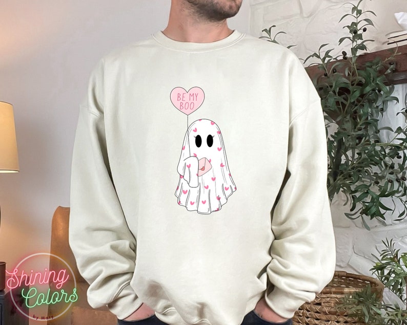 May include: A white sweatshirt with a pink ghost holding a pink heart balloon that says "Be My Boo".