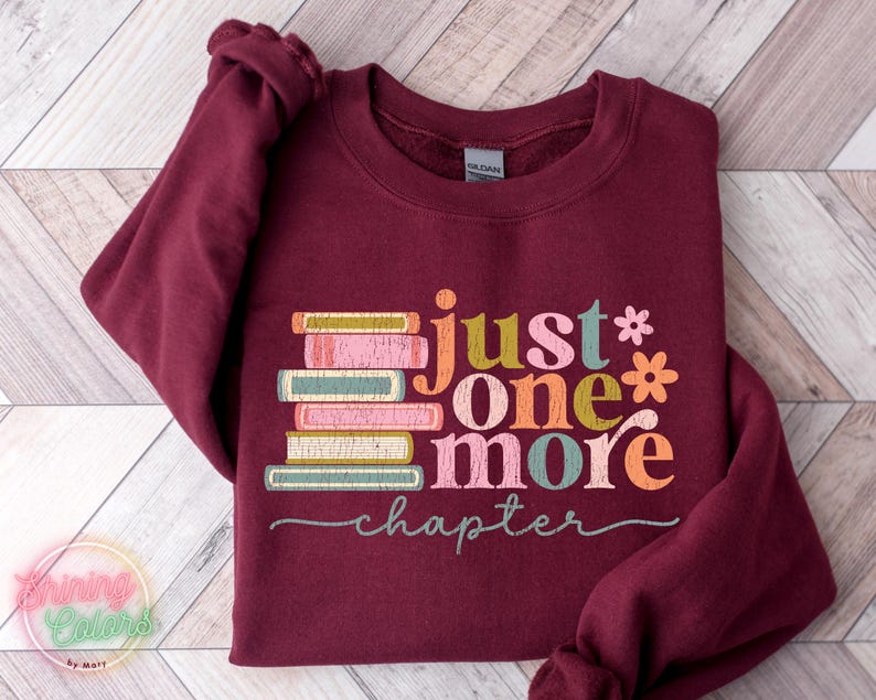 May include: Burgundy sweatshirt featuring a stack of colourful books and the text "just one more chapter" in a retro font.