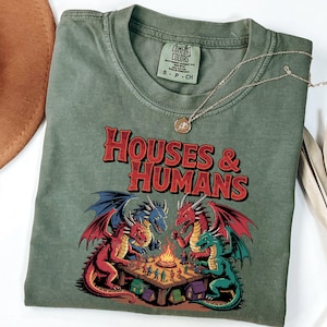 May include: A green t-shirt with a graphic of three dragons playing a game of Dungeons and Dragons. The text "Houses & Humans" is printed in red and white above the dragons.