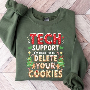 May include: A green sweatshirt with the text "TECH SUPPORT" in red and white, with the phrase "I'M HERE TO DELETE YOUR COOKIES" below. The design includes Christmas tree and gingerbread cookie graphics.