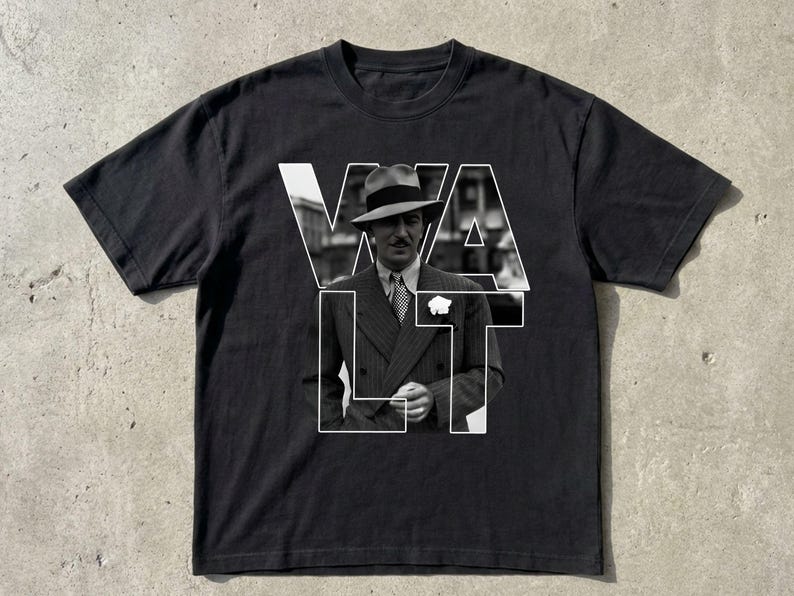Puede incluir: Camiseta negra con una imagen en blanco y negro de un hombre con traje y sombrero, superpuesta con la palabra "WALT" en letras blancas. El hombre lleva un traje y corbata.
