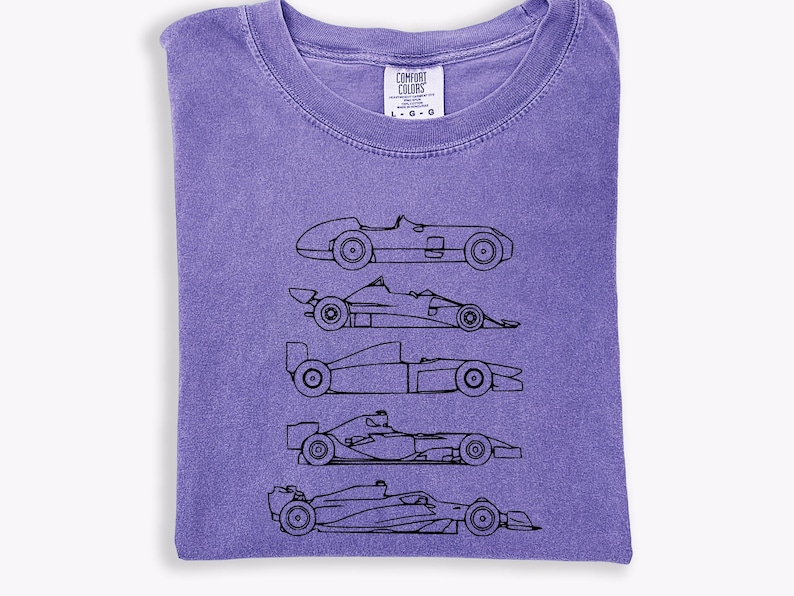 K&ouml;nnte beinhalten: Ein lila Comfort Colors T-Shirt mit einer schwarzen Strichzeichnung von f&uuml;nf Rennwagen. Das T-Shirt hat einen Rundhalsausschnitt und ist gefaltet. Das Etikett lautet "Comfort Colors" und enth&auml;lt Gr&ouml;&szlig;enangaben.