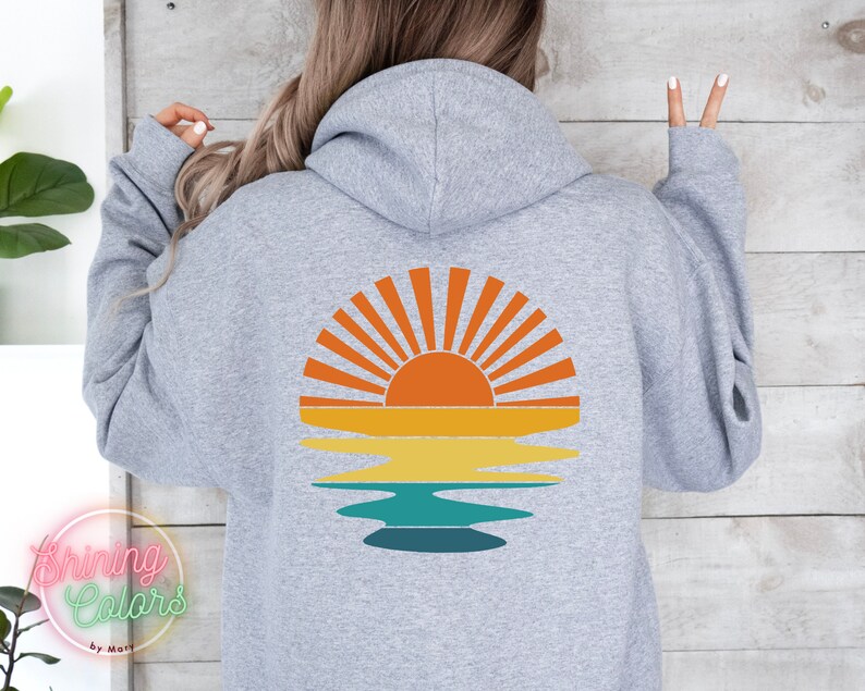 May include: A gray hooded sweatshirt with a retro-style sunset graphic on the back. The graphic features a yellow, orange, and red sun with rays, reflected in a blue and green body of water.
