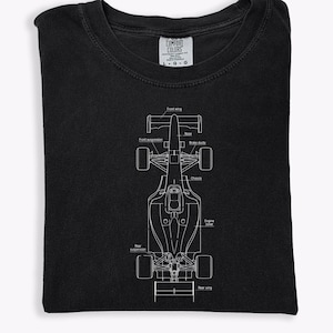 May include: Black t-shirt featuring a white schematic of a Formula 1 race car. The diagram includes labels for the front wing, front suspension, brake ducts, chassis, engine cover, and rear wing. The shirt is folded.