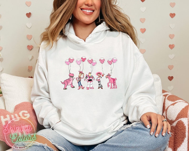 May include: White hoodie with a pink and white graphic of the Toy Story characters holding pink balloons with white polka dots. The characters include Woody, Buzz Lightyear, Jessie, Rex, and Bullseye.