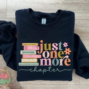 May include: Black sweatshirt featuring a stack of colourful books and the text "Just one more chapter" in a retro font.