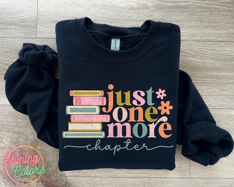 May include: Black sweatshirt featuring a stack of colourful books and the text "Just one more chapter" in a retro font.