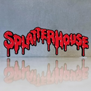 May include: A red "SPLATTERHOUSE" logo with a dripping effect, outlined in black. The logo is reflected on a glossy surface, set against a grey background. The design has a horror theme.