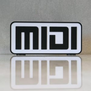 May include: A rectangular sign featuring the word "MIDI" in a bold, sans-serif font. The letters are black against a white background, with a black border. The sign is reflected on a glossy surface.