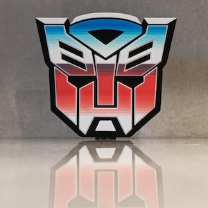 May include: A colourful, stylised emblem featuring a red, white, and blue colour scheme. The design has a black outline and a geometric shape, with a mirrored reflection below. The emblem is likely a logo or symbol.