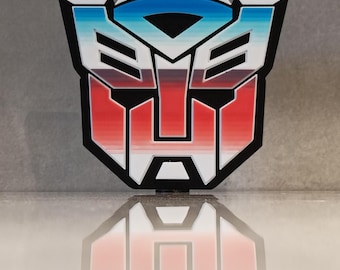 May include: A colorful, stylized emblem featuring a red, white, and blue color scheme. The design has a black outline and a geometric shape, with a mirrored reflection below. The emblem is likely a logo or symbol.