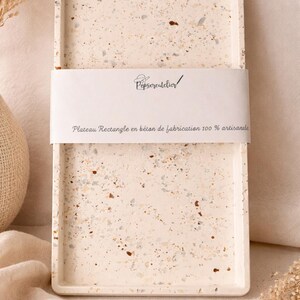 Peut inclure: Plateau rectangulaire en béton beige moucheté. Le plateau a un bord surélevé et une bande blanche avec le texte "Pepscreatelier" et "Plateau Rectangle en béton de fabrication 100 % artisanale". Objet décoratif.