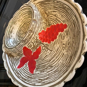 May include: A white ceramic serving dish with a raised rim and a central dip. The dish is decorated with a brown woodgrain pattern and red painted grapes and leaves.