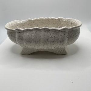 Peut inclure: Pot en céramique blanche avec une finition mouchetée et un bord festonné. Le pot a quatre pieds courts et une forme ovale.